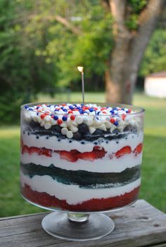 a red, white and blue cake sitting on top of a wooden table next to a tree