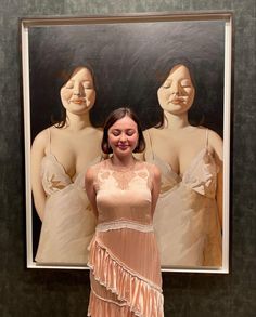 a woman standing in front of a painting with three mannequins behind her