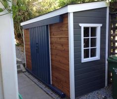 a small shed with a door and window on the side of it next to a trash can