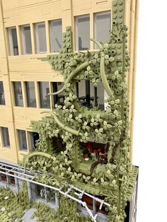 the building is made out of legos and has lots of green plants growing on it