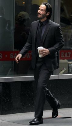 a man in a suit and tie walking down the street with a cup of coffee