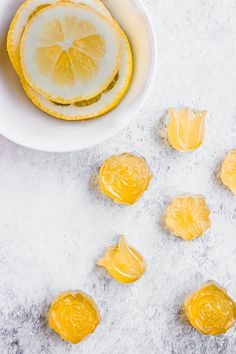 peeled lemons in a white bowl next to a sliced lemon on a gray surface