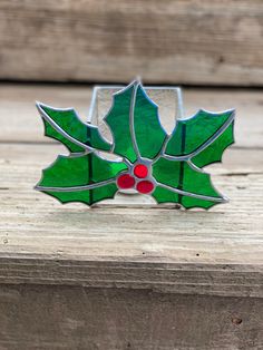 a stained glass christmas leaf brooch with red berries on the center, sitting on a piece of wood