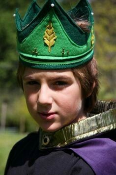 a young boy wearing a green crown and purple shirt with gold trim on his head