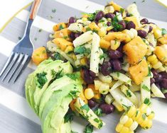 a salad with black beans, corn and avocado on a plate next to a fork