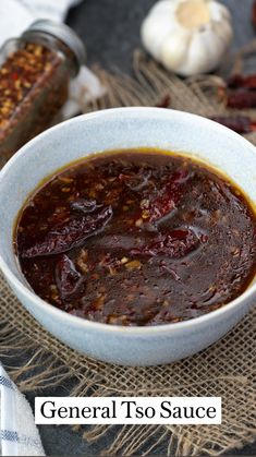 a white bowl filled with chili sauce on top of a table next to garlic and pepper