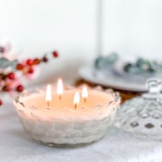 three candles sitting on top of a table next to a glass bowl with red berries