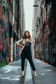 a woman is standing in an alleyway with graffiti on the walls and she has her arms behind her back