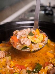 a spoon full of soup with meat, vegetables and spices in it is being lifted from the crockpot