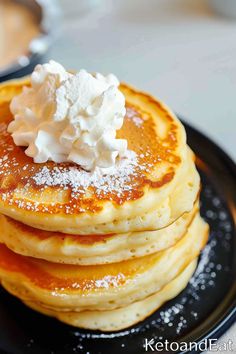 stack of pancakes topped with whipped cream on a black plate, ready to be eaten