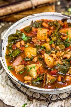 a white bowl filled with beans and greens on top of a wooden table next to bread