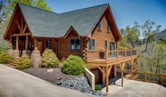 a large log cabin with a deck on the front and side of it, surrounded by trees