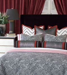 a bed with red and black pillows in front of a window