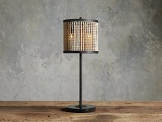 a table lamp with beads on it sitting on top of a wooden table next to a concrete wall