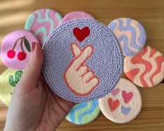 a hand is holding a small patch with different designs on it and the button has a red heart