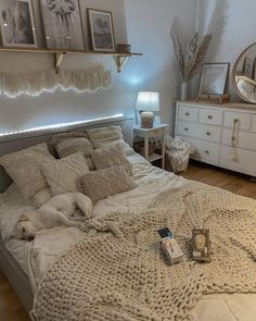 a bedroom with a bed, dressers and pictures on the wall above it is lit by lights