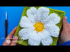 a crocheted square with a white and yellow flower on it, next to a crochet hook