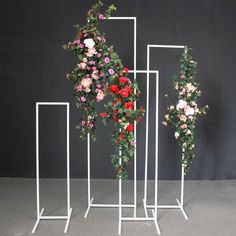 three white stands with flowers on them against a black wall and one has pink, red and purple roses in it