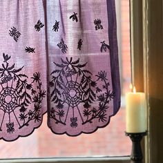 a candle is lit in front of two curtains with spider webs and flowers on them