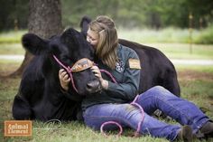 a woman is petting a black cow in the grass with her pink rope around it's neck