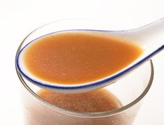 a spoon full of liquid sitting on top of a glass filled with something orange and brown