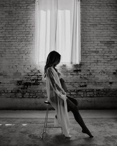 a pregnant woman sitting on a chair in front of a brick wall with a window