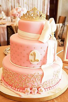 a pink and white wedding cake with gold decorations on it's sides, sitting on top of a table