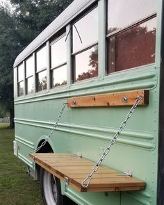 a green school bus with a wooden bench attached to it's front door and windows