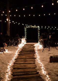 an outdoor ceremony with candles and lights on the snow covered path that leads up to the entrance