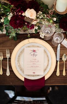 the table is set with white and gold plates, silverware, and red napkins