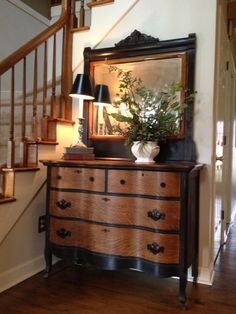 a wooden dresser sitting under a stair case next to a mirror and lamp on top of it