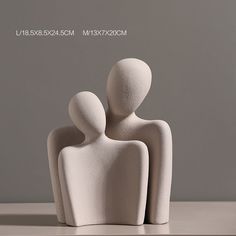 two white sculptures sitting on top of a table next to each other in front of a gray background