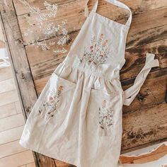 a white apron with flowers on it sitting on top of a wooden table next to a phone