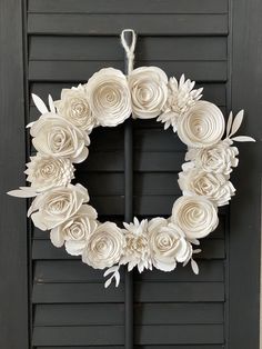 a wreath made out of paper flowers hanging on a black door with shutters in the background