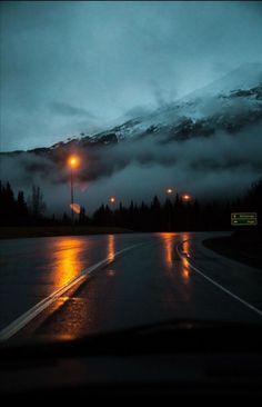 the rain is pouring down on the mountains and street lights in front of them at night