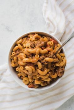 a white bowl filled with pasta and meat on top of a table next to a striped towel