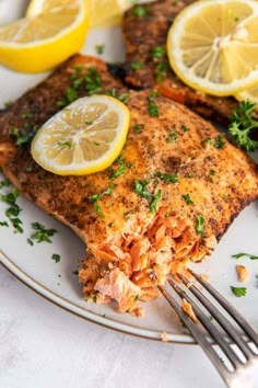 a white plate topped with fish covered in lemons and parsley next to a fork