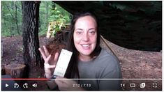 a woman holding up a box in front of a tree with her hand on it