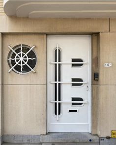 a white door on the side of a building with a round window and metal bars