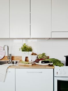 a kitchen with white cupboards and counter tops has vegetables on the cutting board, as well as a potted plant