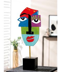 a colorful mask is on top of a black stand in front of a white wall