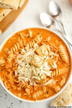 a bowl of pasta soup with bread and parmesan croutons on the side