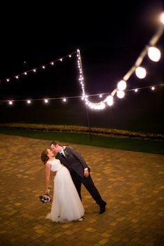 a bride and groom kissing in front of string lights