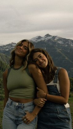 two women standing next to each other in front of mountains