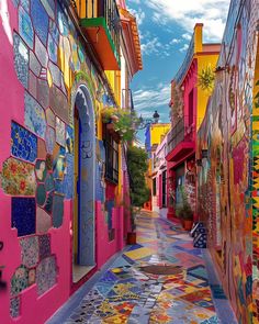 an alleyway with brightly colored buildings and colorful mosaic tiles on the walls, along with potted plants