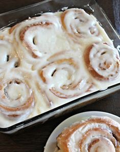 two plates with cinnamon rolls on them next to a baking pan filled with the same kind of doughnuts