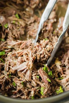 two tongs are sticking out of shredded meat in a bowl with parsley on the side