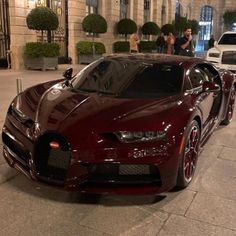 a red bugatti parked on the side of a street next to other cars