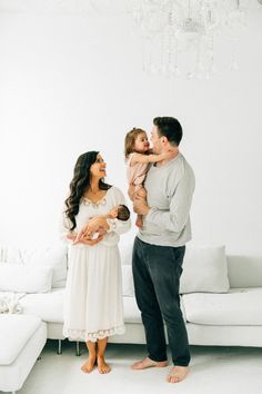 a man and woman holding a baby while standing in front of a white couch