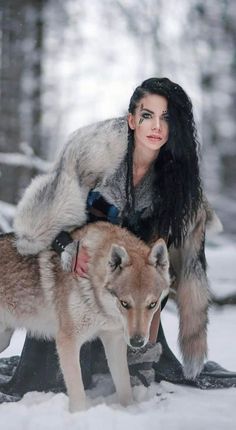 a woman with black hair is sitting on a wolf in the snow and holding it's tail